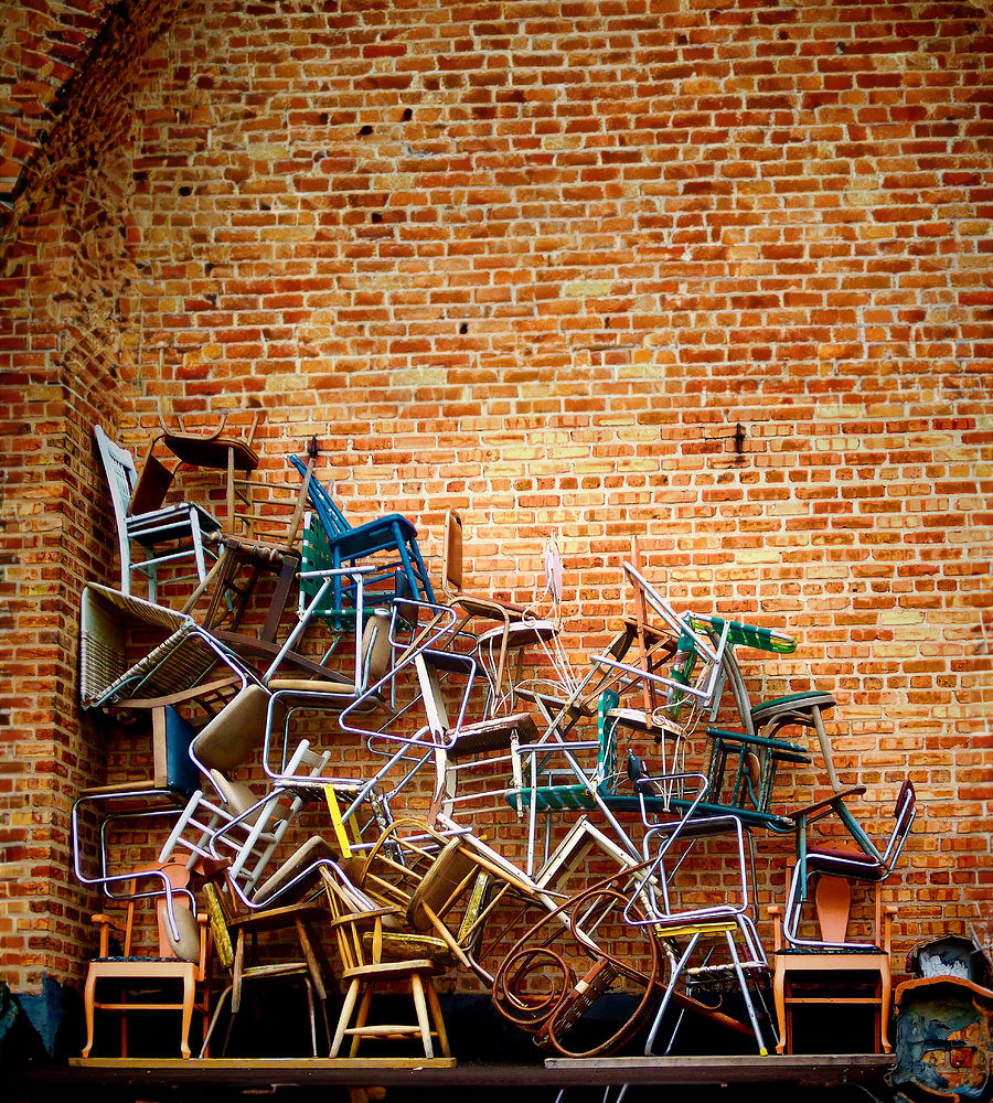 a stack of colorful chairs arrangled into a pile against a brick wall.